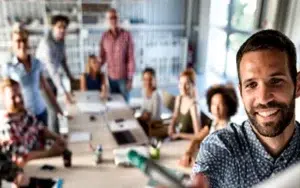 Business Project Management Fundamentals 10 Smiling professional in front of a team meeting at a long table