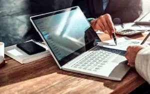 Microsoft Office Excel Basic: Unlock Spreadsheet Essentials 17 Colleagues reviewing a report on a laptop with pens and a calculator