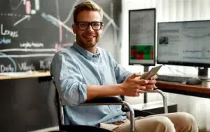 Microsoft Power BI: Data Analysis for Professionals 20 Smiling professional in a wheelchair holding a phone beside data monitors