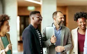 Assertive Communication Skills: How to Speak Up Effectively at Work 13 Diverse coworkers smiling and talking in an office corridor