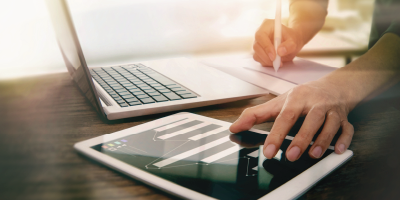 An individual analyzing data from an ipad while working on the laptop