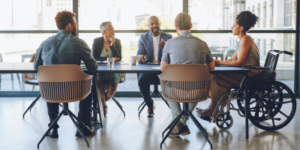 Disability, diversity and business meeting with staff, people or team communication, planning on corporate strategy, goal or mission for KPI. Woman in wheelchair in group talking of company inclusion. - Managing Up