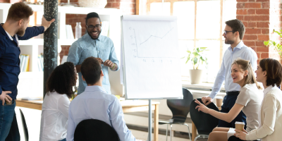 Smiling African American mentor or coach make flipchart presentation for diverse employees, excited black presenter present project on whiteboard, coworkers laugh having fun at casual briefing - Principles of Critical Thinking