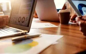 Data Analytics Fundamentals Series: From Beginner to Analyst 7 Laptop showing charts next to printed reports and coffee on a desk