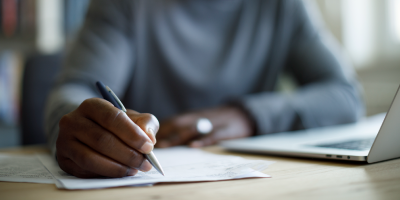 A man is working at his desk, writing technical information.