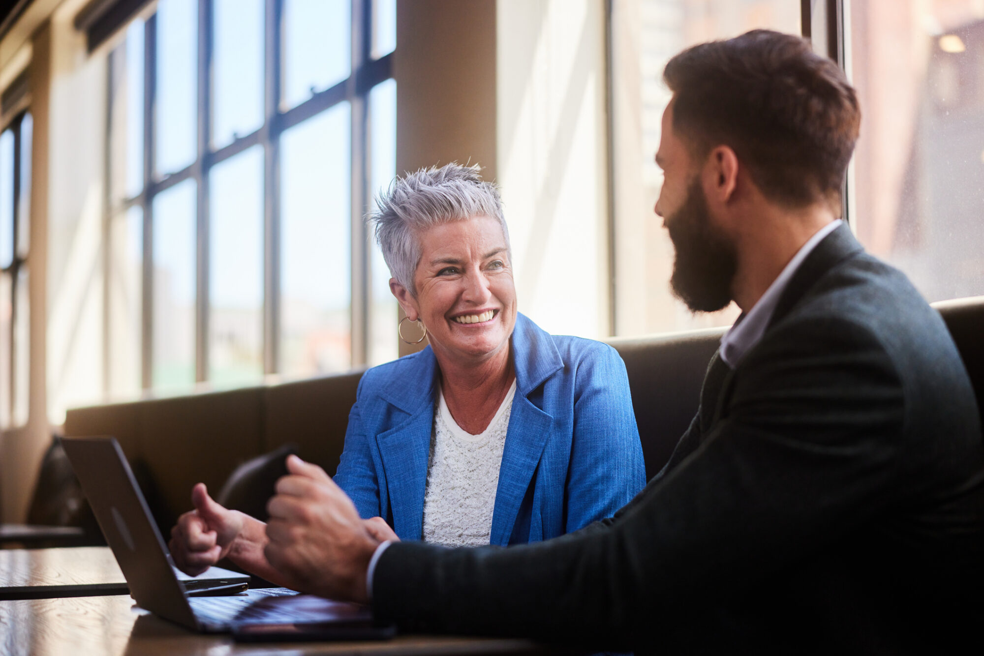 Smiling businesswoman mentoring a young colleague over a laptop in a workplace meeting.