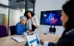 AI for Emotional Intelligence & Workplace Relationships 14 Business professionals collaborating in a meeting using laptops and artificial intelligence tools to improve teamwork and productivity.