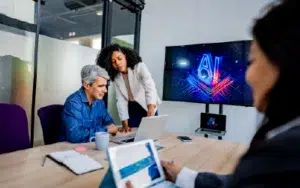 AI for Emotional Intelligence & Workplace Relationships 17 Business professionals collaborating in a meeting using laptops and artificial intelligence tools to improve teamwork and productivity.