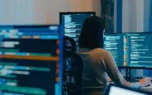 Super Intelligence and Machine Learning Essentials for Federal Employees 38 Developer working at multiple monitors displaying code in a dim office